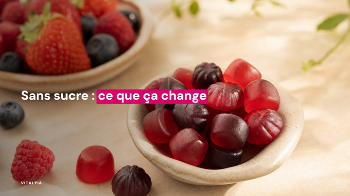 Des gummies rouges et noirs dans une coupelle en céramique sur une table crème, avec des fruits rouges en arrière-plan.
