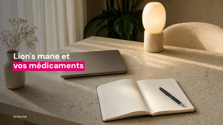 Un bureau avec un carnet ouvert, un stylo, un ordinateur portable fermé, une lampe allumée et un vase avec des fleurs séchées