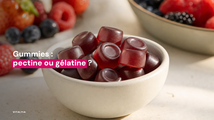 Des gummies rouges dans une coupelle blanche sur une table avec des fruits rouges en arrière-plan.