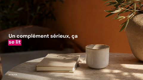 Un carnet et une tasse en céramique sur une table en pierre avec un vase et des plantes.